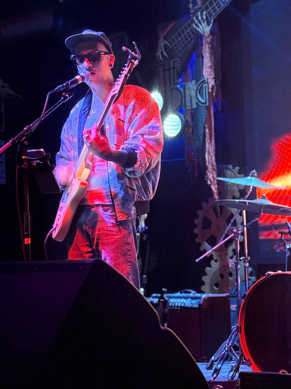 Jeremy Dean performing live onstage with sunset visuals behind him.